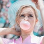 Woman with blonde hair and sun hat blowing a bubble gum